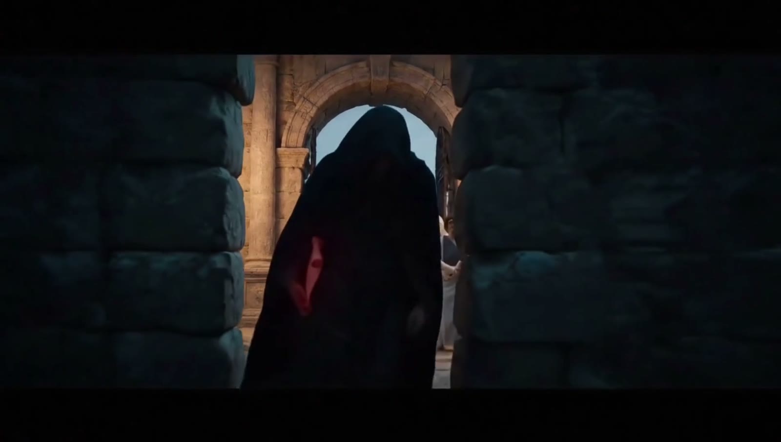 A hooded figure slips through a gap in the wall